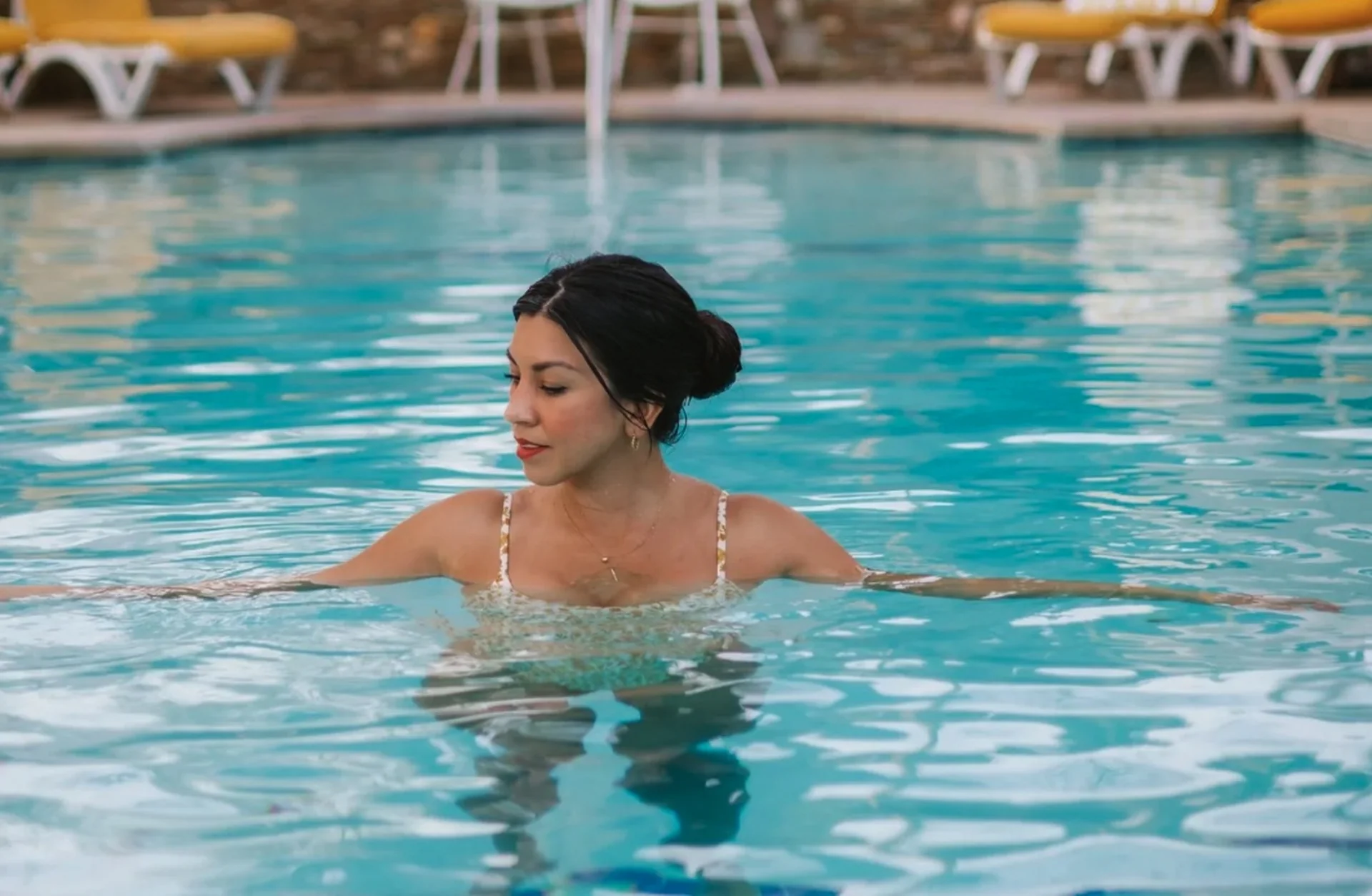 Woman soaking in mineral pool surrounded by yellow lounge chairs