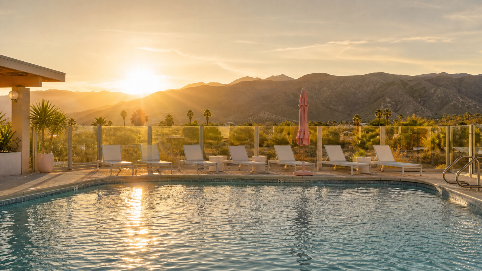 Azure Palms pool at golden hour with lounge chairs, a pink umbrella, glass fence, and desert mountains
