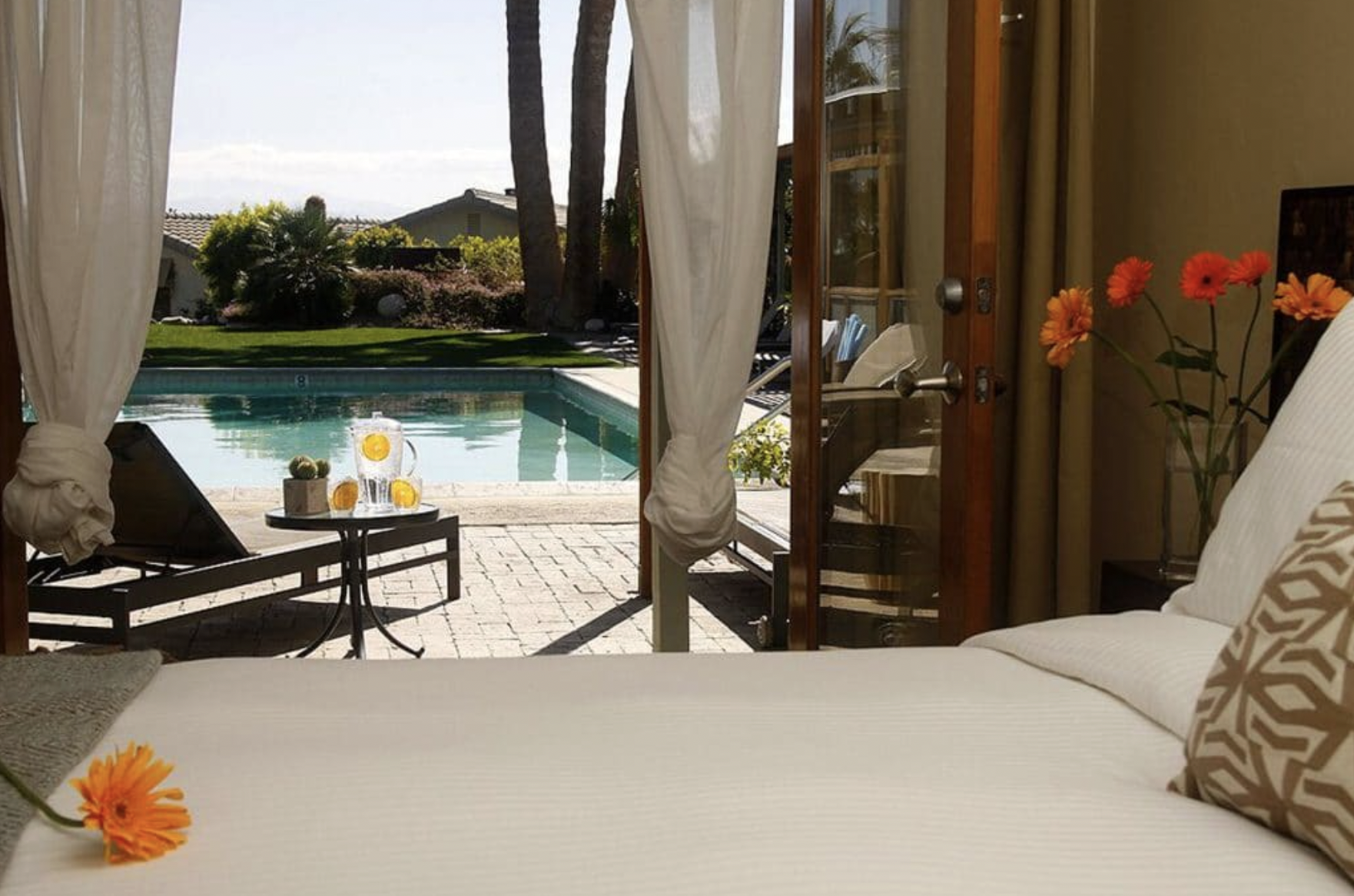 Cabana day-bed view through curtains to a private poolside lounge with chilled lemon water at a Desert Hot Springs spa