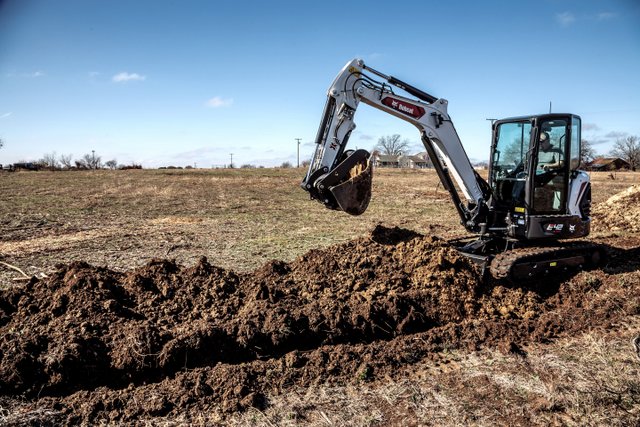 Compact excavator clearing agricultural field with dirt piles visible