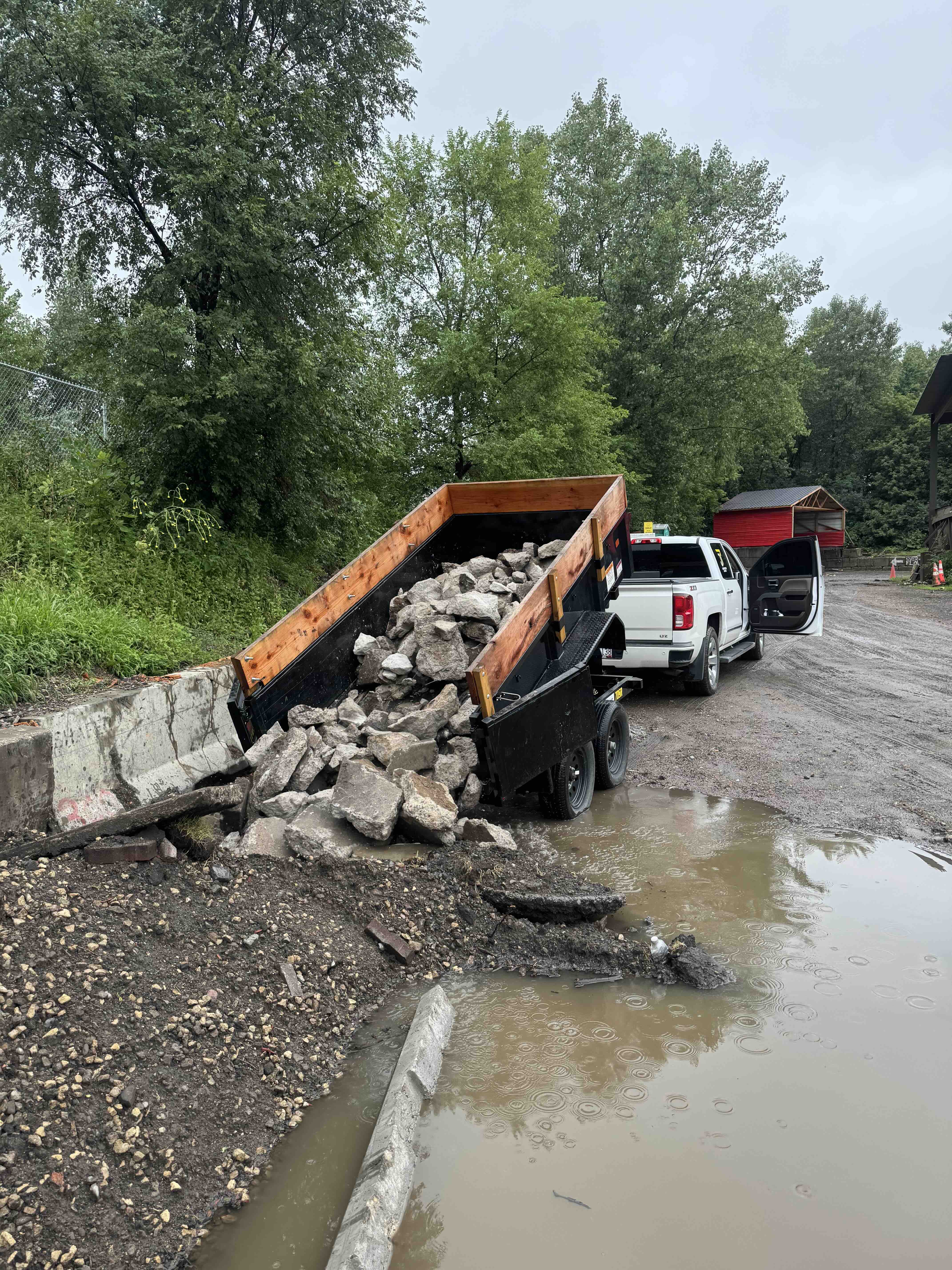Red compact track loader transporting large boulders alongside a waterway