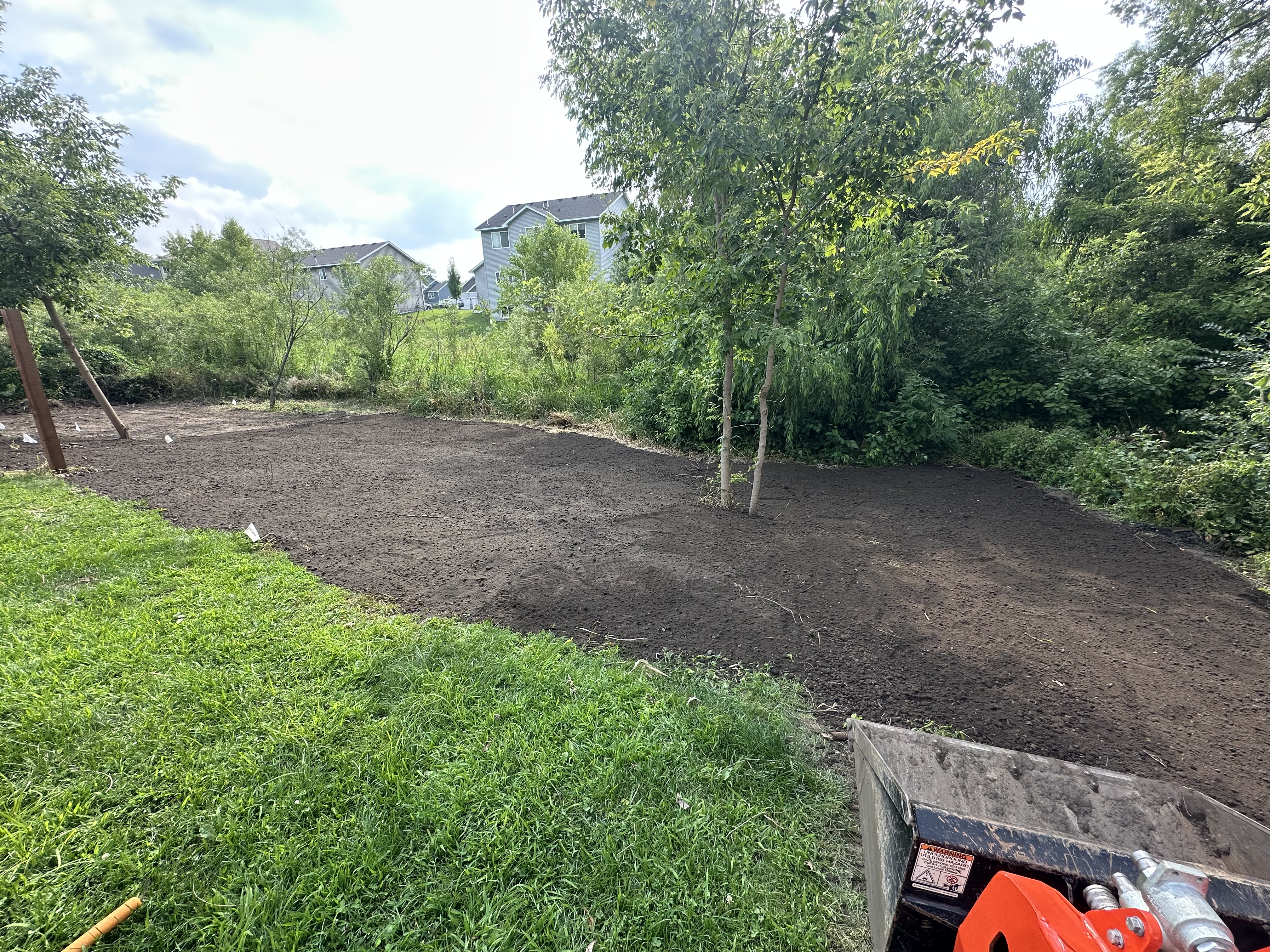 Cleared and leveled site with retained trees and residential homes visible