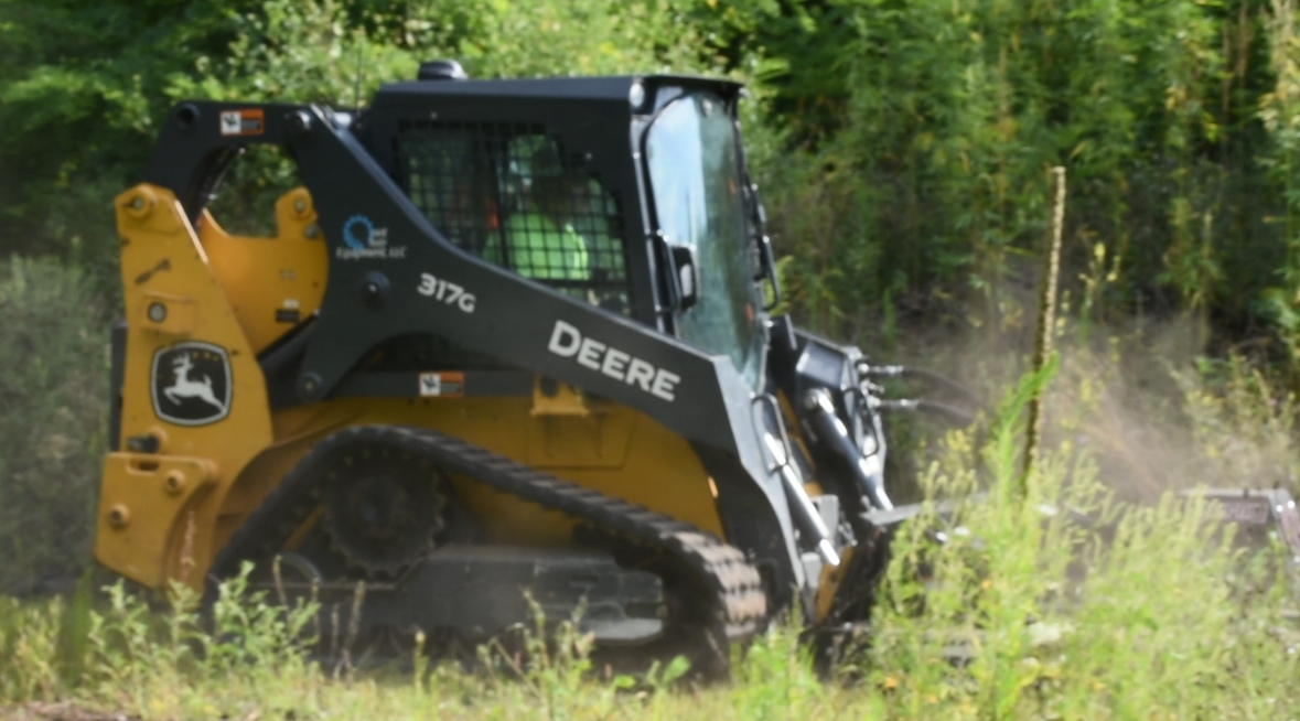 John Deere skid steer with brush clearing attachment working in wooded area