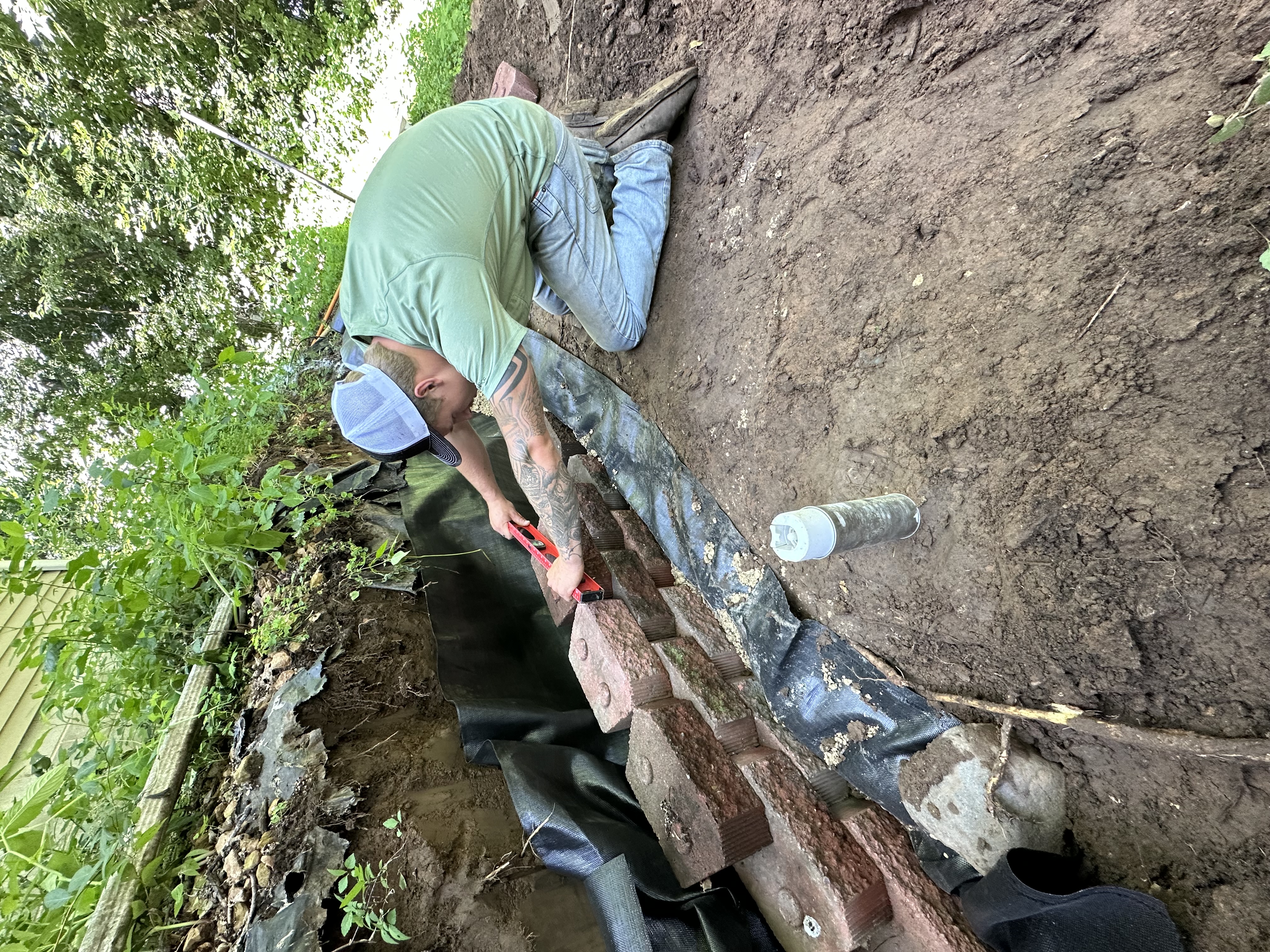 Workers installing black drainage pipe in freshly dug trench