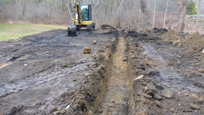 Yellow excavator digging a drainage trench in muddy conditions